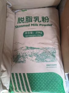 Bag of skimmed milk powder, net weight 25 kg, beige with green Chinese text and a mountain illustration.
