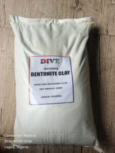 Bag of natural bentonite clay on a wooden floor, label reads 'DIVE NATURAL BENTONITE CLAY' (25 kg, Nigeria).